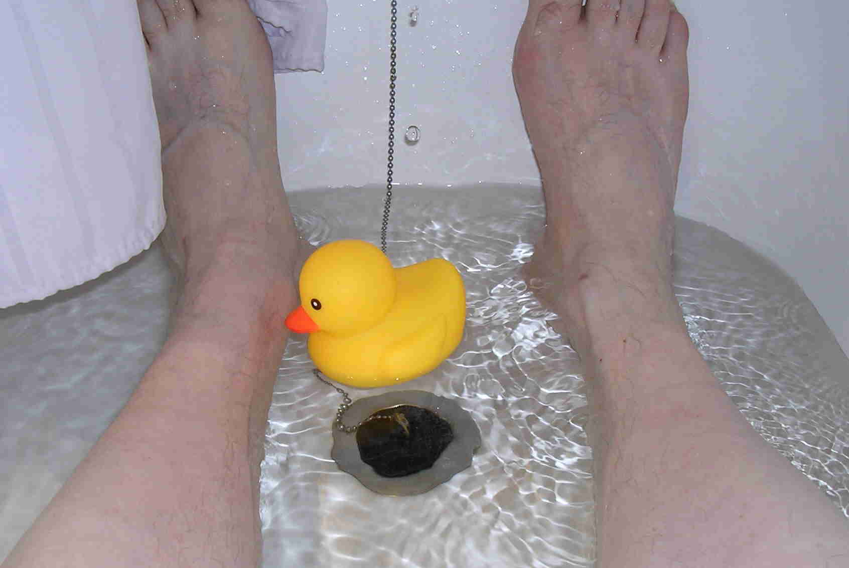 Bath with water, a pair of feet and a floating rubber duck